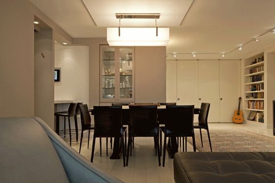 Dining area with a long dark table and black chairs under a rectangular pendant, with built-in shelving behind