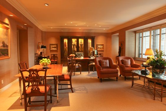 Room with warm lighting, grasscloth walls, upholstered armchairs, a dining table and a wooden display cabinet