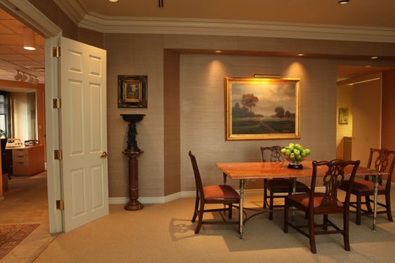 Room with grasscloth walls, a framed landscape painting and a wooden table with chairs, seen through open double doors