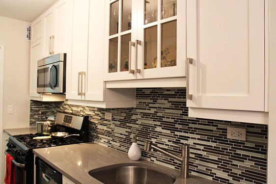 Kitchen with white shaker cabinets, glass-front uppers, a linear glass-tile backsplash and stainless steel appliances