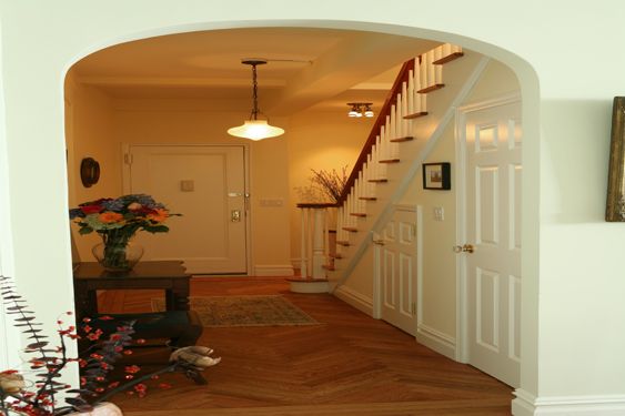 Arched entry hall with a herringbone wood floor, a pendant light and a white staircase