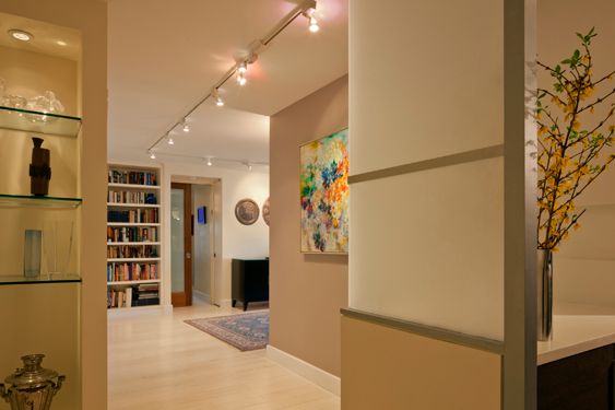Hallway with track lighting and glass display shelves leading to built-in bookcases