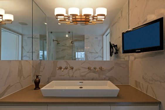 Bathroom with marble-look walls, a rectangular vessel sink, wall-mounted brass faucets and a glass shower
