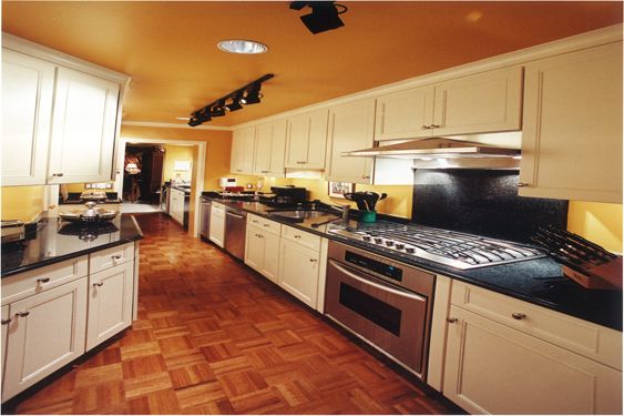 Galley kitchen with cream cabinets, black countertops, a stainless steel range and parquet floor